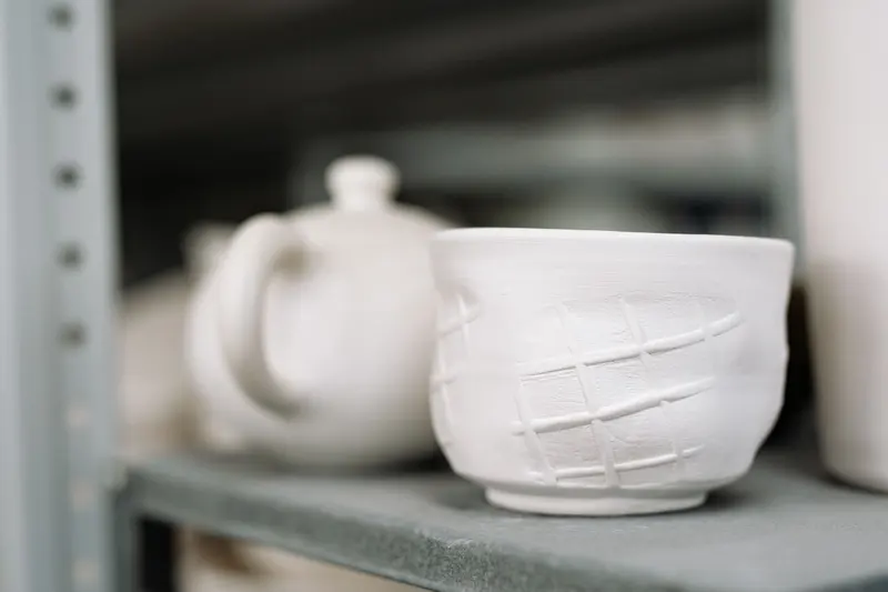 Pale handmade pottery on studio shelves, the kind of work a clay shrinkage calculator helps you size before it dries and fires.