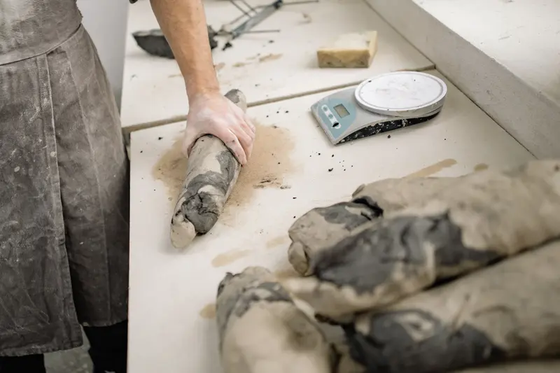 A potter rolling clay beside a kitchen scale on the workbench, weighing out portions the way a clay weight calculator suggests.