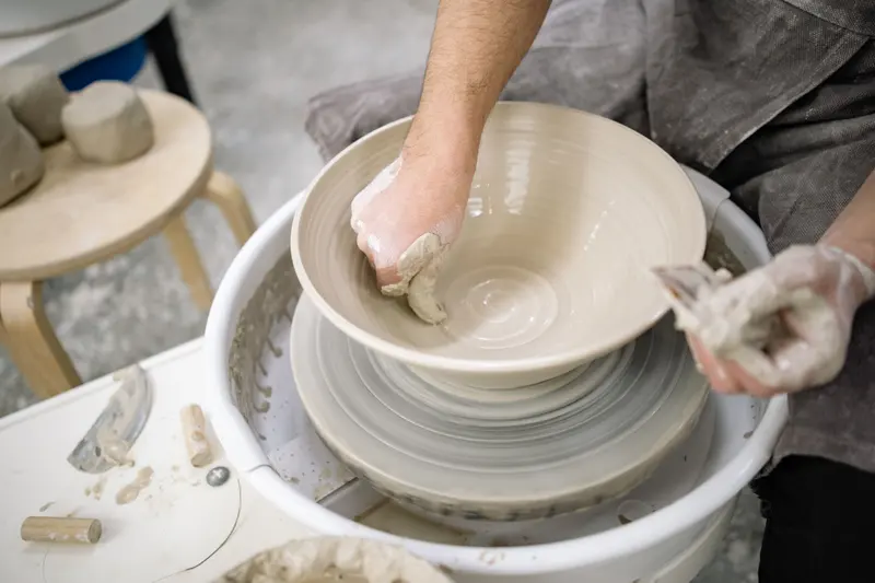 A potter throwing a bowl on the wheel from a weighed ball of clay, the starting weight a clay weight calculator works out.