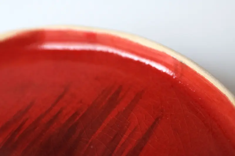 Close-up of a glossy red glaze on the curved edge of a ceramic plate.