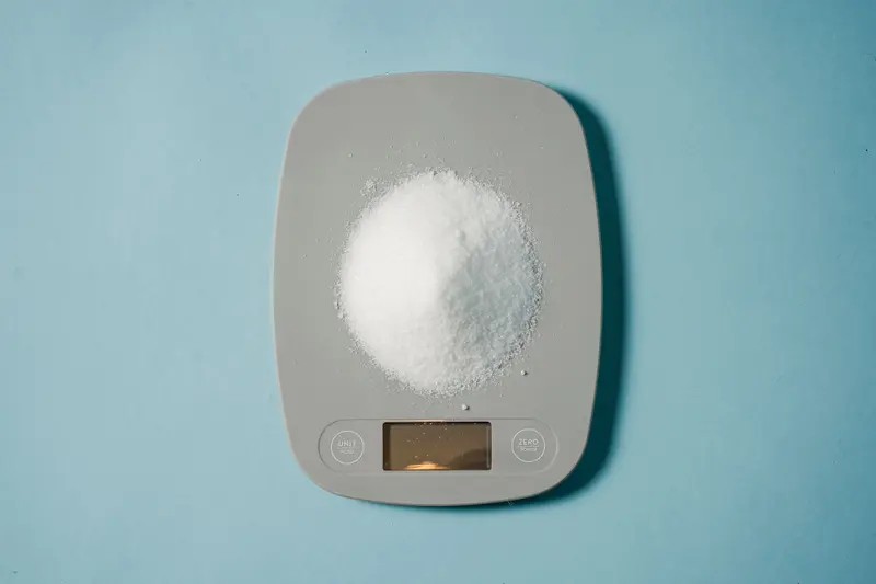 A small mound of white powder on a digital kitchen scale against a blue background.