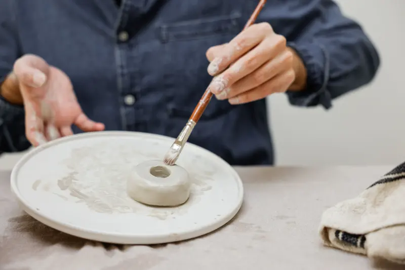 An artisan carefully applying colour to a handmade clay piece, the careful coats Mayco glaze combinations call for.