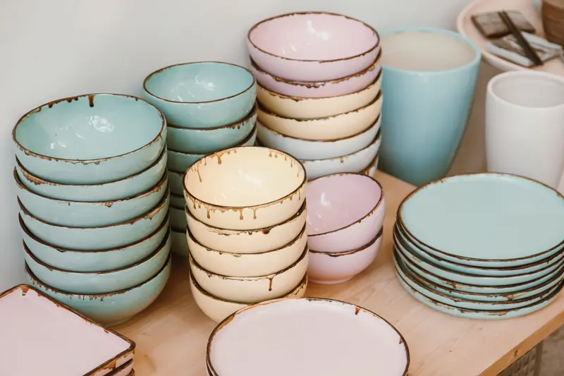 Pastel glazed bowls and plates stacked on wood, soft colours like some Mayco glaze combinations.
