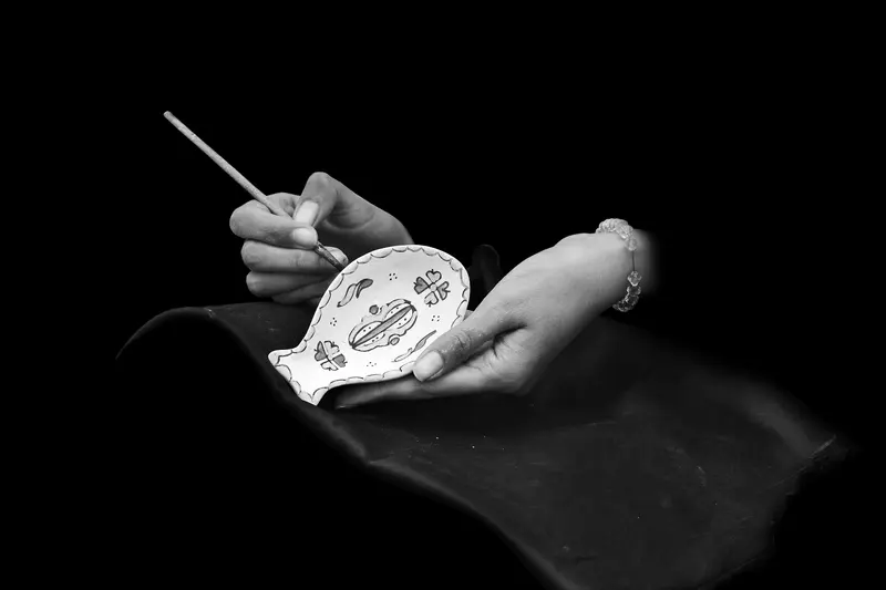 Hands painting a ceramic plate with a fine brush, the kind of detail Speedball underglaze is made for.
