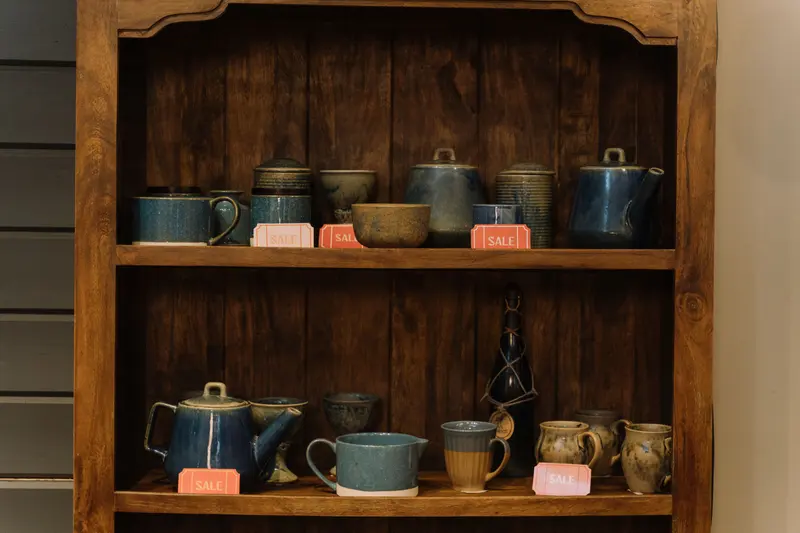 Handmade pottery cups and teapots on a shelf with sale tags, priced using a pottery pricing method.