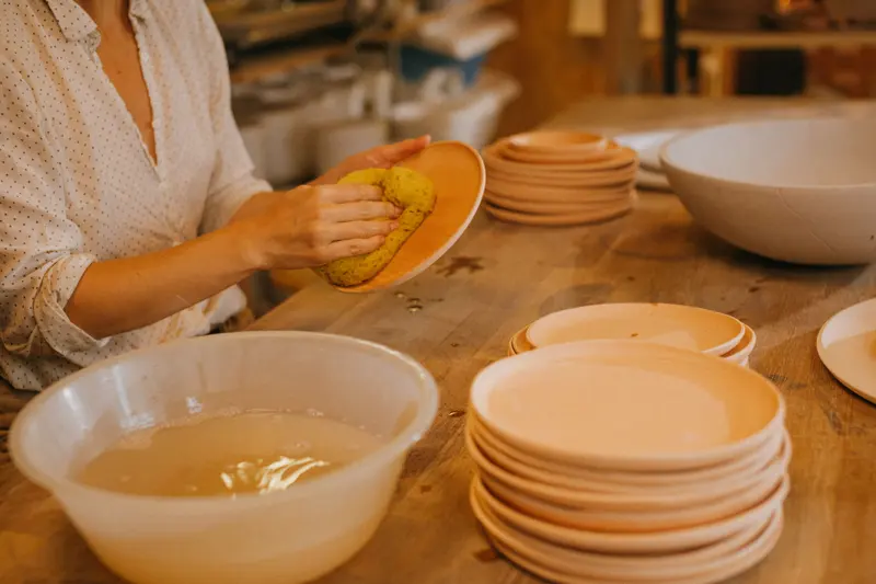 A potter wiping bisque-fired plates before glazing, ware that sits low on the pyrometric cone chart at around cone 06.