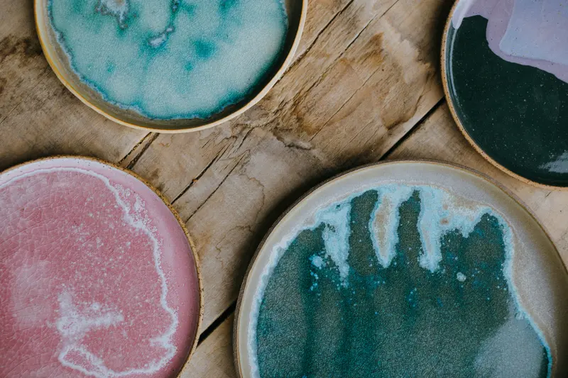 Glazed stoneware plates in flowing teal, pink and green glazes, the kind of result a pyrometric cone chart helps you fire for.