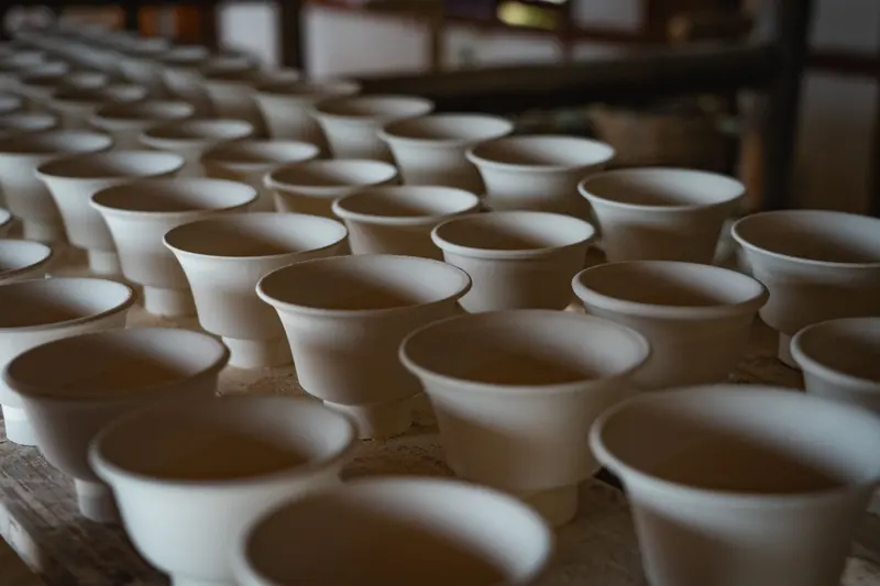 Rows of identical white unglazed cups on a workshop table.