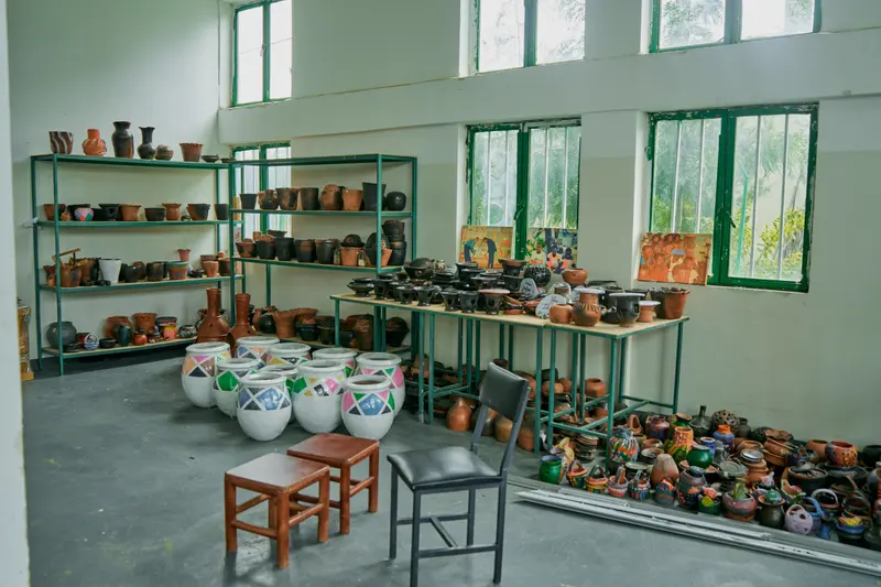 A pottery workroom with handmade pots and vases on shelves and tables beside large windows.