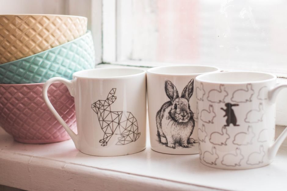 Ceramic mugs with decorative decal designs displayed on a shelf