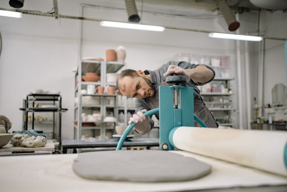 Artist using a slab roller for pottery in a studio environment