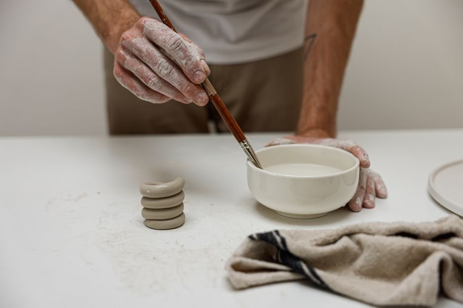 Artist hand painting a ceramic bowl with underglaze detail using a fine brush
