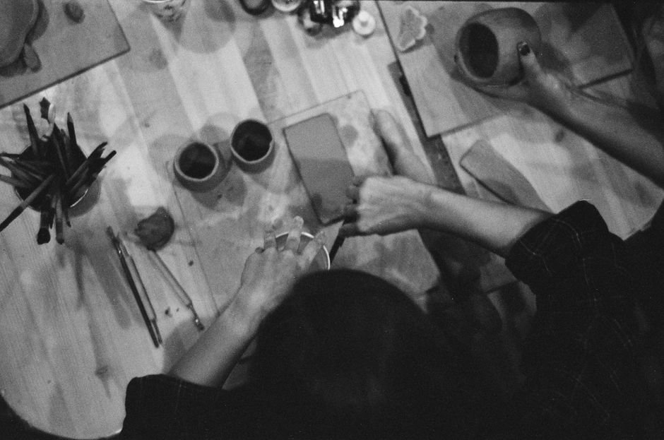 Hands crafting pottery with detail tools shown from above in black and white