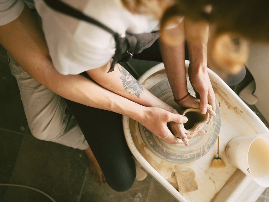 Two people shaping clay on a pottery wheel, the kind of experience offered by pottery wheel classes near you