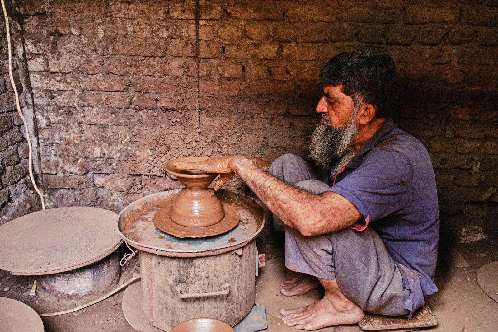 Potter pulling clay walls upward during the throwing stage on a wheel