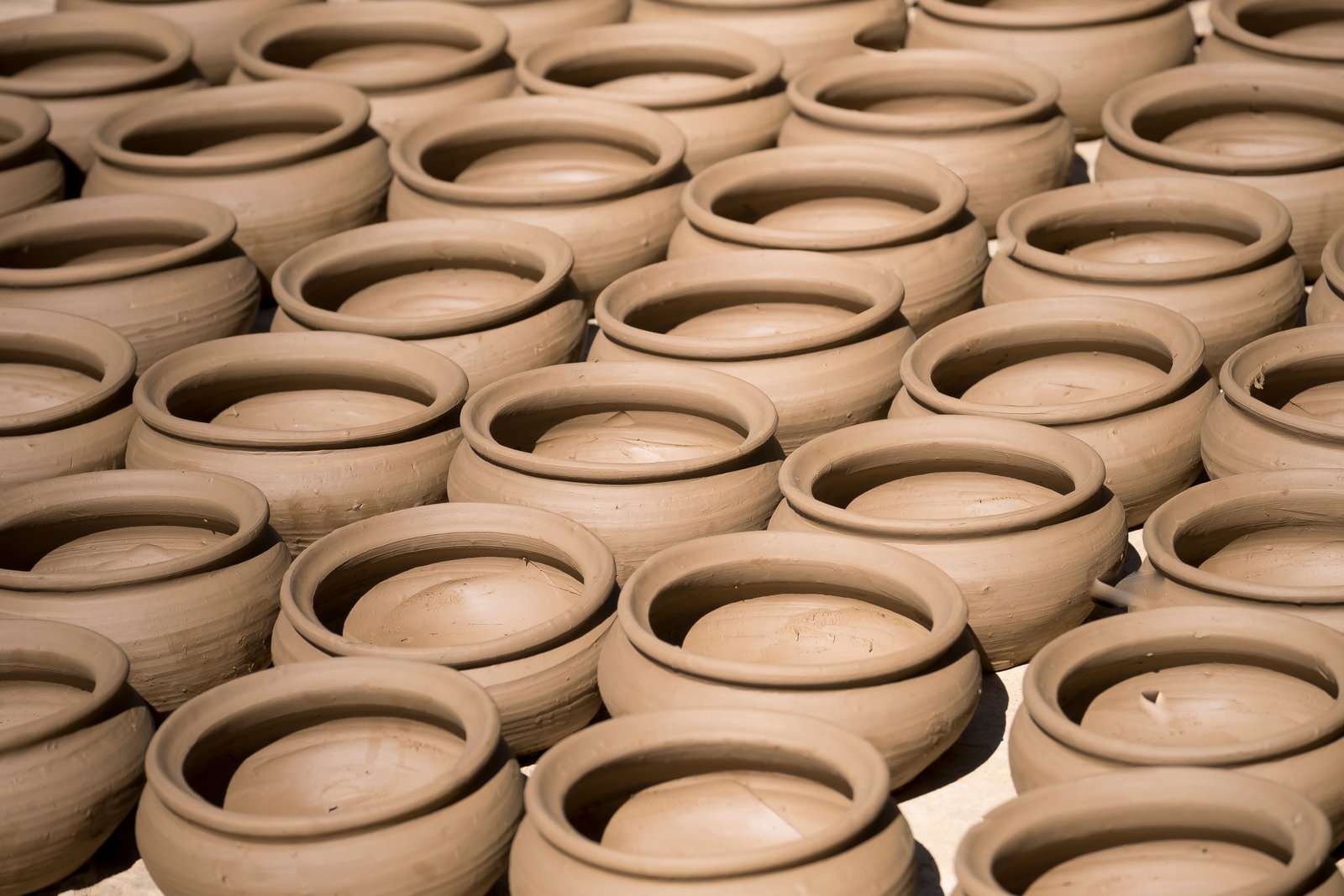 Rows of similar handmade pottery forms drying in a studio