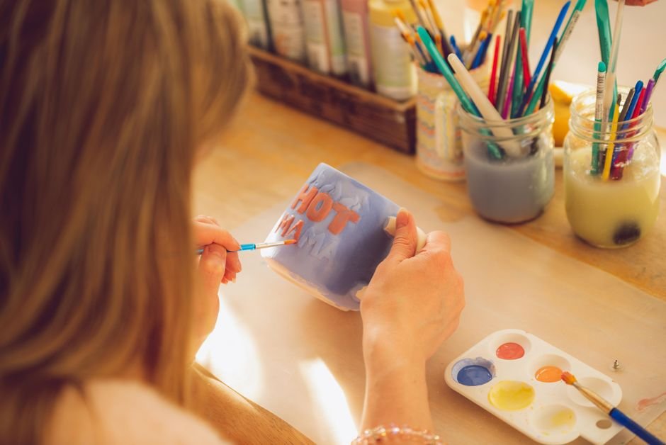 Woman painting a mug in a studio, turning unpainted ceramics into a personal piece