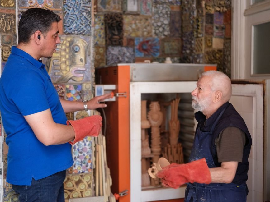 Two potters talking in a ceramic workshop with a kiln, weighing up buying a kiln vs a community studio