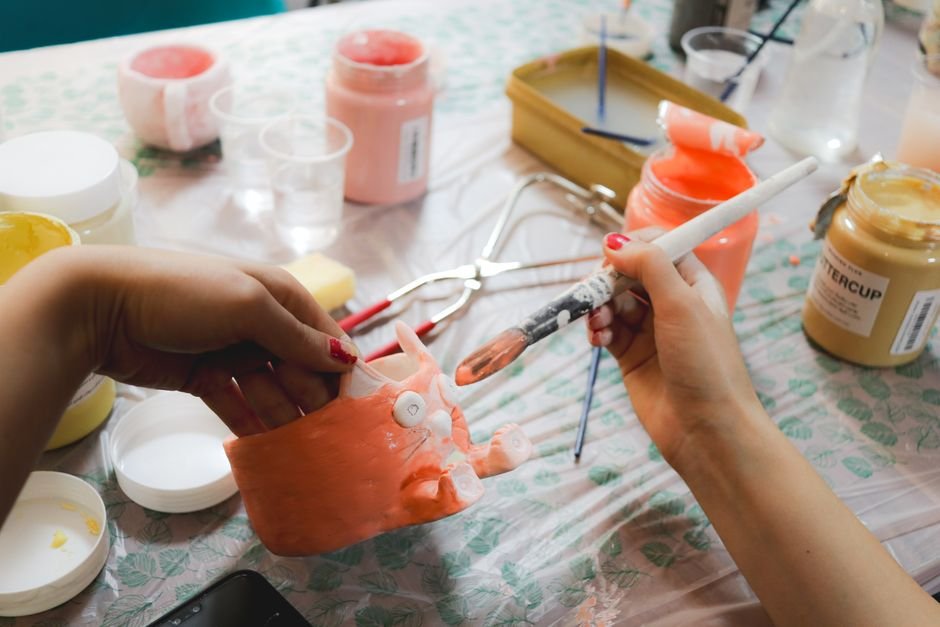 Hands painting pottery at an indoor workshop, an alternative to buying ceramic painting kits