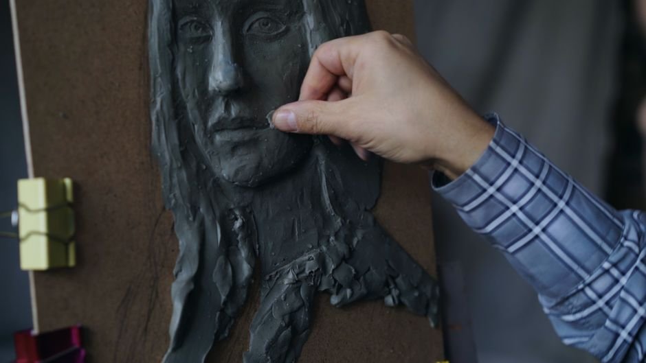 Artist sculpting a clay face on a wooden board, an early stage of ceramic sculpture
