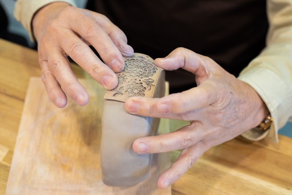 Hands molding and decorating a clay pot, a stage where many hand building mistakes beginners make appear