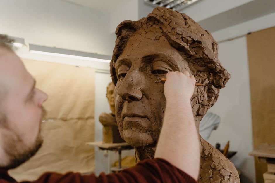 Artist refining a clay bust with a loop tool, one of the essential clay sculpting tools