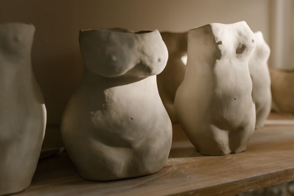 Handcrafted ceramic sculpture of human forms on a wooden shelf
