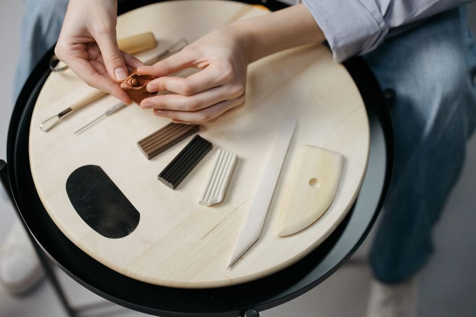 Hands working clay with clay sculpting tools on a wooden board