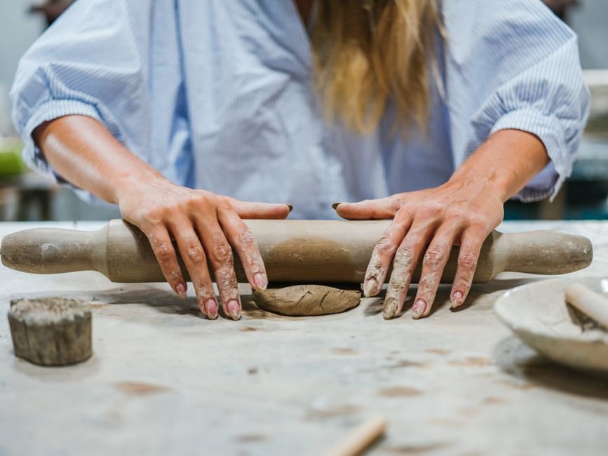 Hands rolling clay with a rolling pin to prepare a slab for slab hand building methods