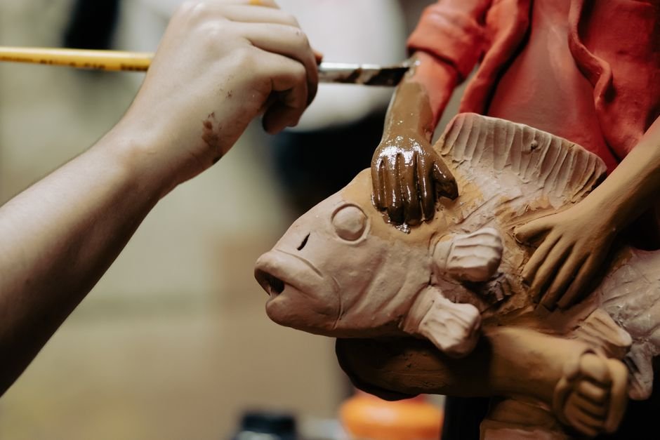 Artisan painting a clay sculpture with a fish design, a step many ceramic painting kits imitate at home