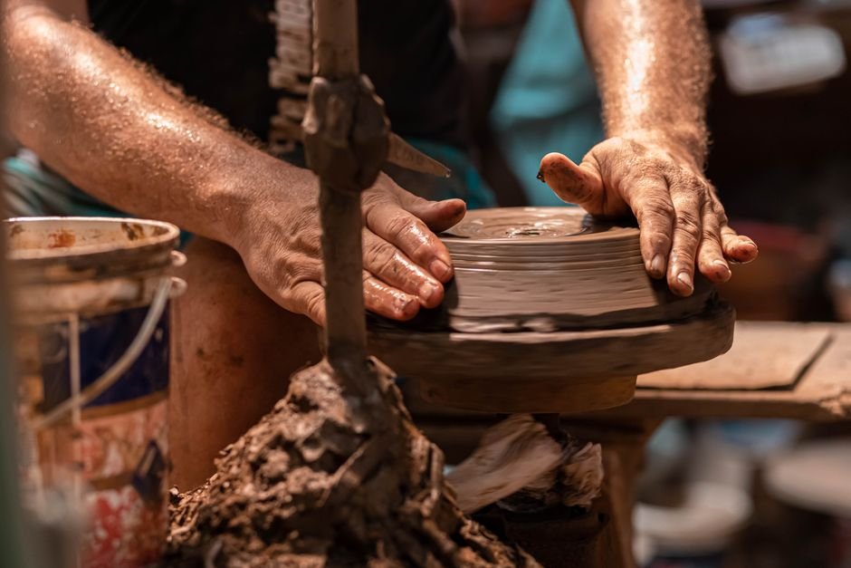 Potter's hands shaping a clay pot on a spinning wheel, working carefully to avoid a pot collapsing