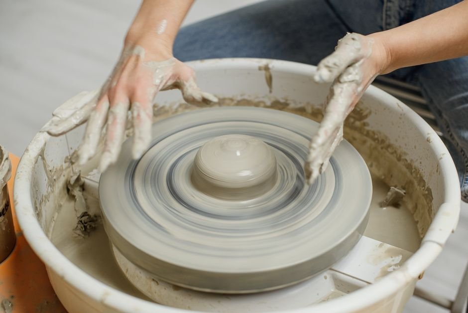 Hands shaping clay on a pottery wheel, illustrating ceramic definitions like centring and throwing