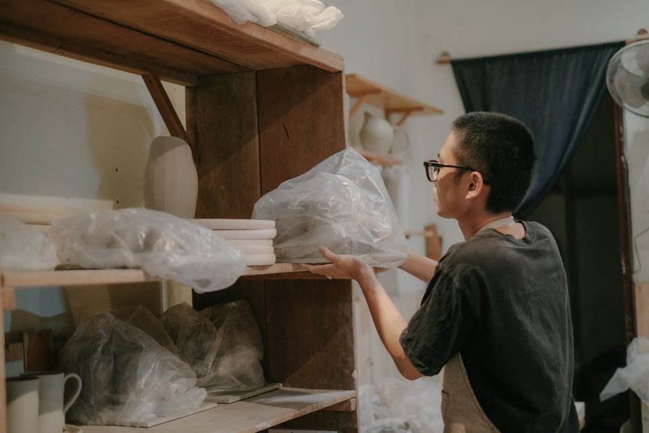 Artisan arranging handcrafted pottery on studio shelves, part of the day to day work behind many ceramic jobs