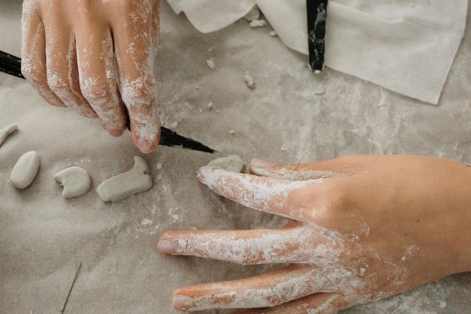 Hands sculpting small clay pieces, the first step in making what is a figurine by hand