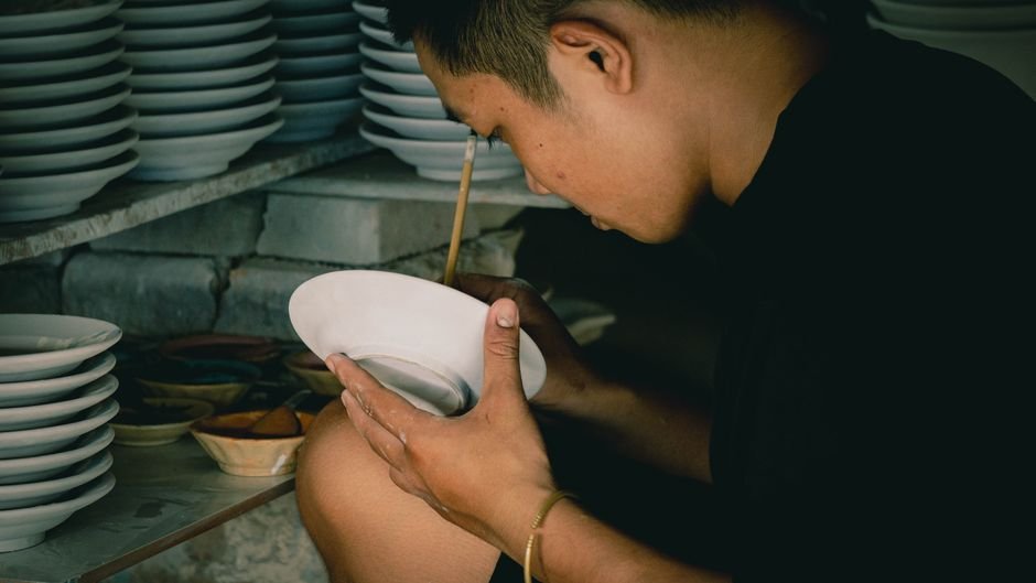 Artisan hand painting a ceramic plate, the step just before learning what happens after paint your own pottery