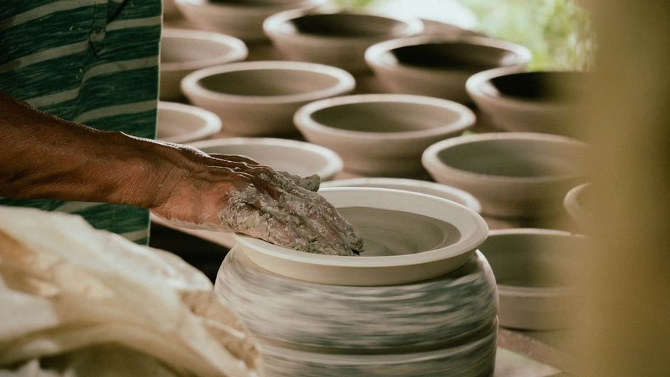 Hands shaping a pot on a wheel, the first stage of the pottery studio journey from wet clay to finished piece