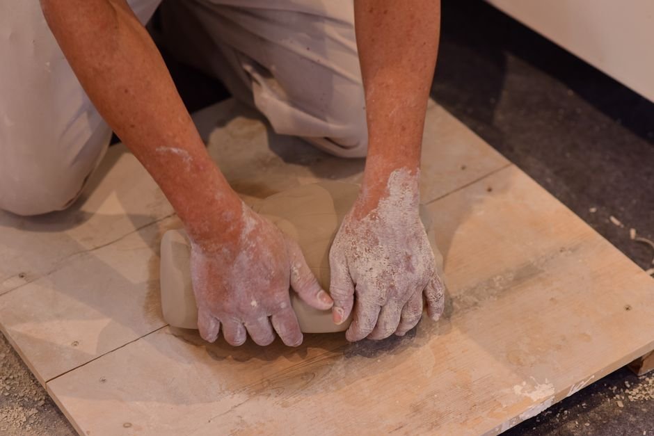 Hands kneading sculpting clay on a wooden board before starting a piece