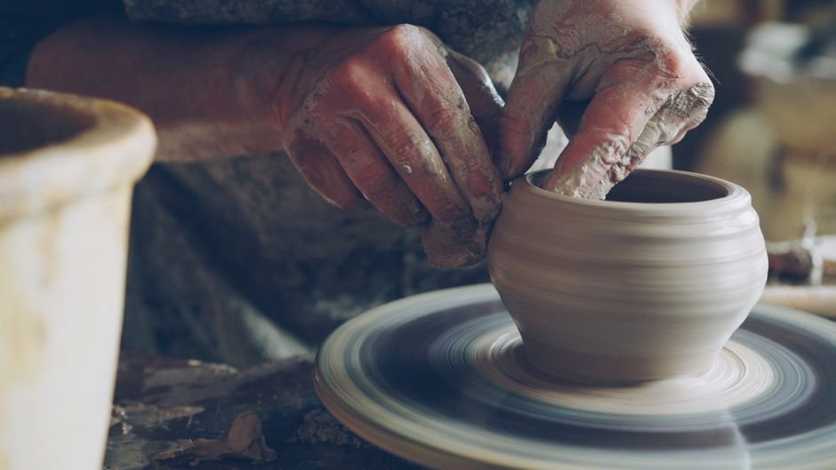 Potter shaping clay on a spinning wheel, one side of the wheel throwing vs hand building choice