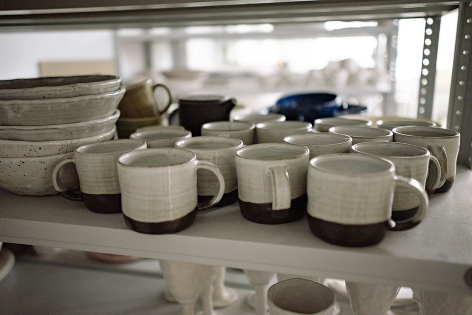 Finished glazed mugs on a studio shelf, showing what happens after paint your own pottery once pieces are fired