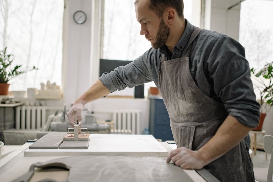 Craftsman smoothing handmade clay tiles in a workshop, making unglazed ceramic tile by hand
