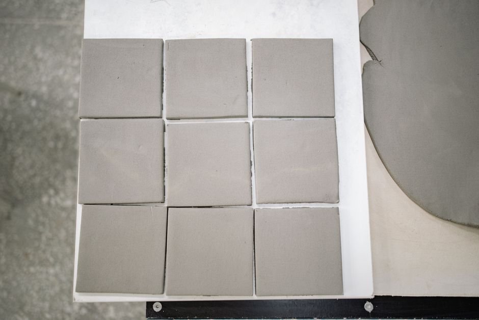 Freshly cut square clay tiles on a workshop table, like those used in a ceramic materials workshop