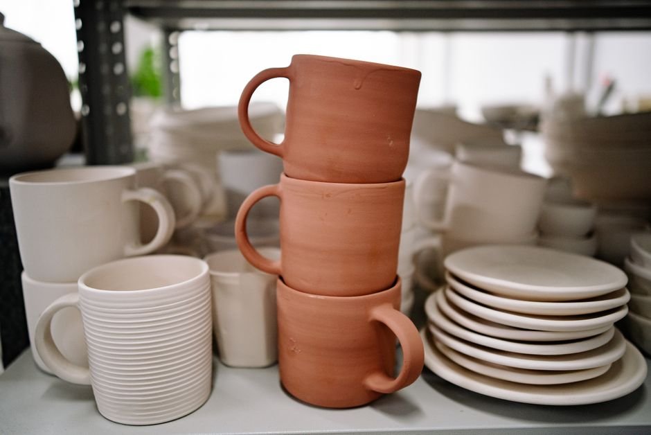 Stacked handmade mugs and plates in a studio, the consistent range a pottery business relies on
