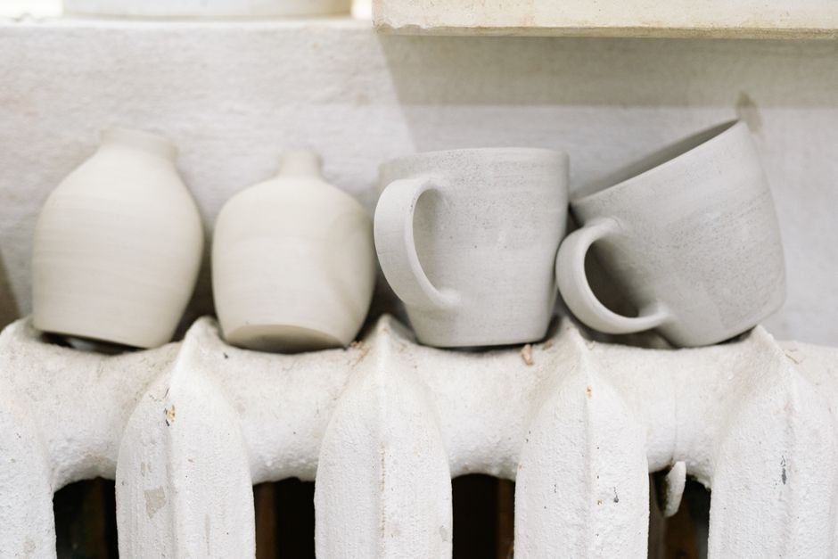 Handmade mugs and vases drying in a pottery studio, a common sight with greenware ceramics