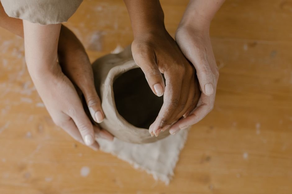 Several hands shaping clay pottery on a wooden table during beginner ceramics projects