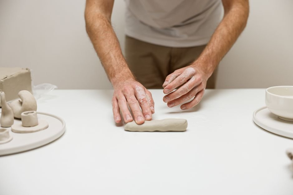 Person working clay by hand at a pottery workshop table, preparing clay as you would with a wedge tool