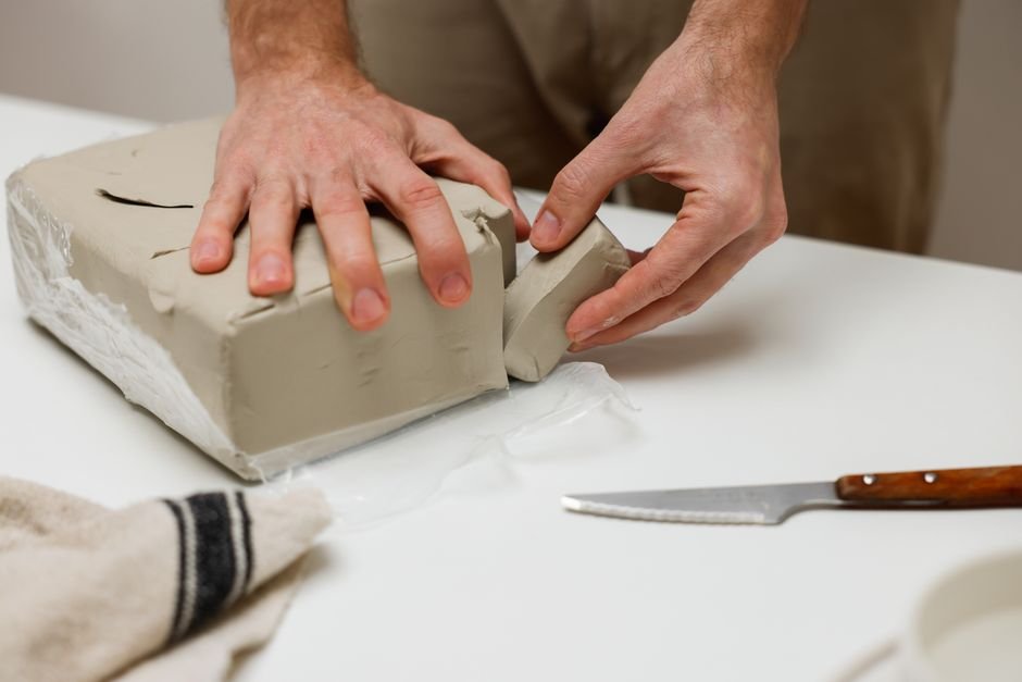 Hands shaping a block of prepared clay on a table, the end point of how is clay made