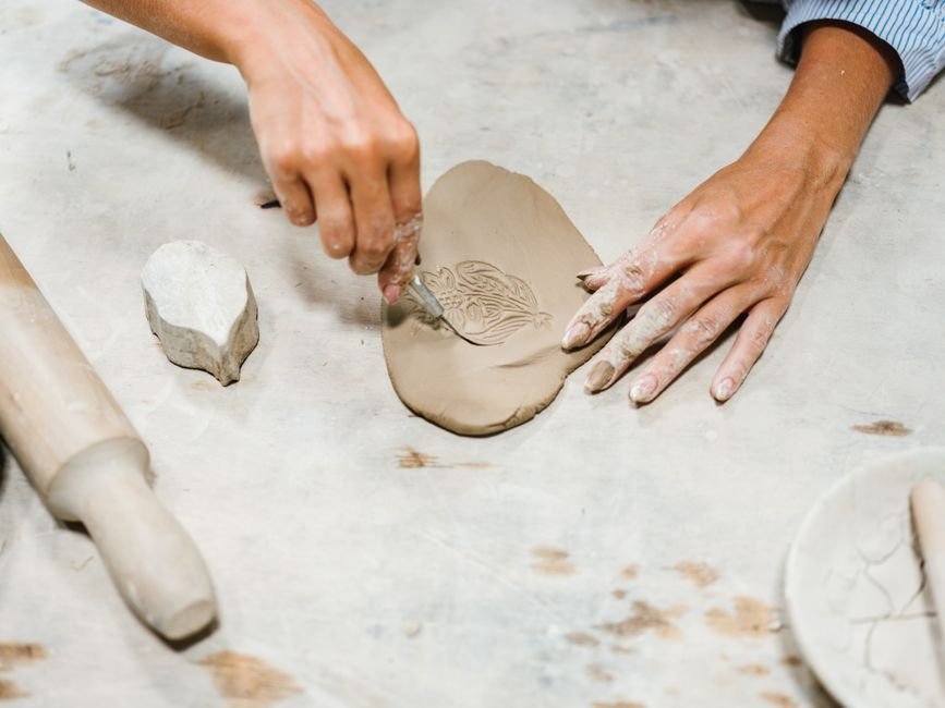 Hands working clay with small tools on a worktable, the kind of detail work used in sprigging