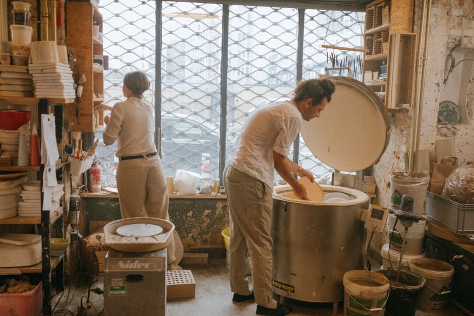 Makers working in a shared pottery workspace, where many weigh up an electric kiln vs gas kiln